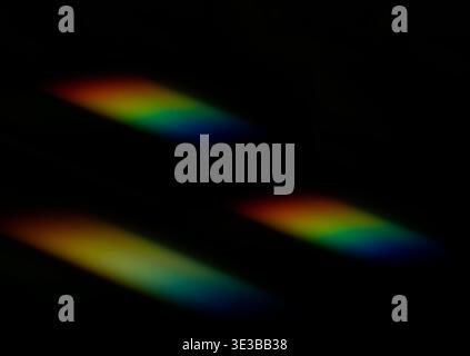 Soft diagonal streaks of rainbow light glow against a deep black background, creating a minimal abstract composition with vibrant color gradients. Stock Photo