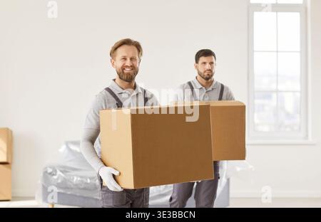 Mover team working together, two men wearing work uniforms are carrying cardboard boxes in room  Stock Photo