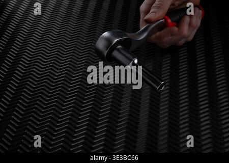 Close up of hand holding ratchet wrench with attached socket extension over dark textured background. Mechanical tool prepared and ready for use in wo Stock Photo