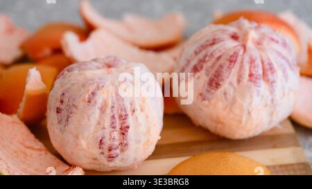 Two peeled whole grapefruits on a wooden cutting board surrounded by pieces of citrus peel. Close-up Stock Photo