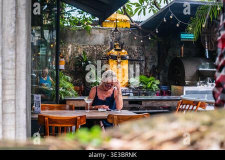 Middle-Aged Woman Checking Phone at an Outdoor Balinese Cafe Stock Photo