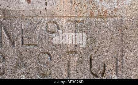 Close-up of a weathered concrete wall featuring faint carved letters and rough surface texture. Shows aged material, subtle typography detail, and nat Stock Photo