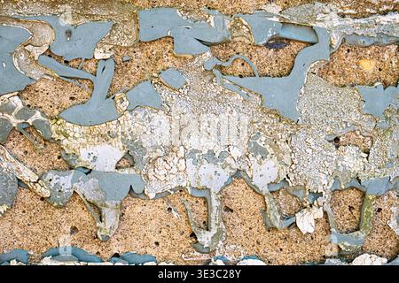 Close-up of cracked and peeling paint on a weathered concrete wall, revealing layered textures and rough surface details. Stock Photo