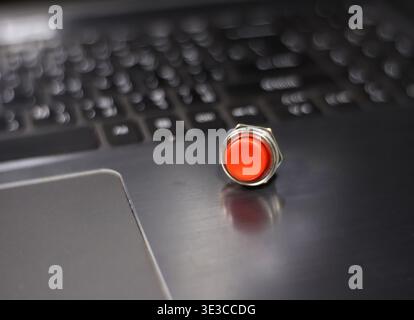A red push button is placed on a laptop keyboard. Stock Photo