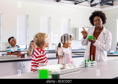African American teacher in lab coat holding green beaker, teaching goggled kids in lab, copy space Stock Photo