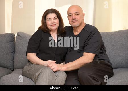 A man and woman sit together on a couch holding hands indoors. Stock Photo