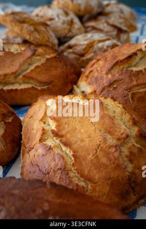 Rustic homemade folar or Easter bread with golden-brown crust and chewy texture resting on a cloth, warm from oven in natural daylight. Close-up shot Stock Photo