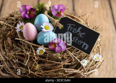 Happy Easter - Easter basket with colorful Easter eggs and spring flowers on rustic wood - German text for Happy Easter Stock Photo