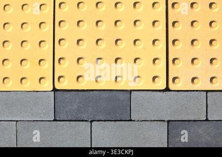 Yellow concrete paving slabs with convexed points. Special tactile paving slab with ribbed surface for blind people. Cover of grey rectangular paving Stock Photo