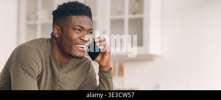 Mobile communication. Happy handsome black man talking on cellphone in kitchen Stock Photo
