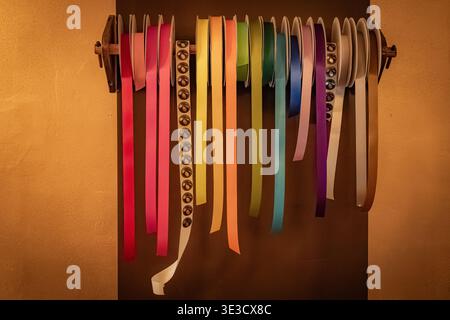A collection of colorful satin ribbons, including a patterned one, hangs from spools on a rustic wooden wall rack against a textured brown background Stock Photo