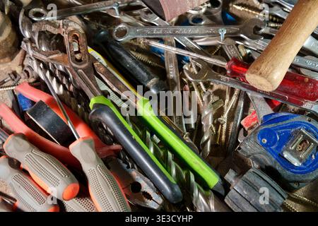 Top view close-up of a messy, cluttered assortment of used hand tools including wrenches, pliers, screwdrivers, drill bits, and a measuring tape Stock Photo