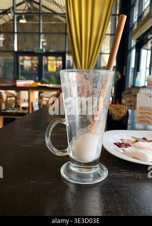 Empty glass with a wooden stirrer on a dark wooden table in a cafe, with blurred background of seating and decorative elements visible Stock Photo