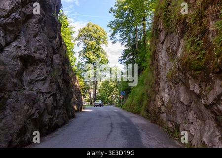 Car driving on a narrow asphalt road between high rocky cliffs leading to Lechfall in Fussen, Germany. Summer Alpine landscape with green forest and s Stock Photo