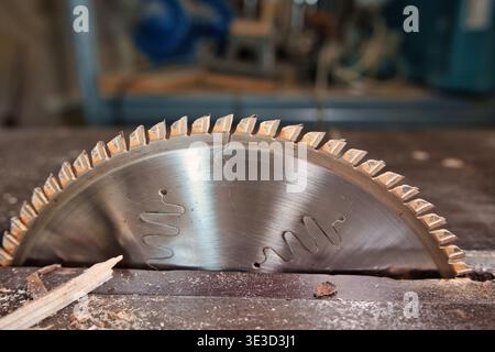 Close-up of a circular saw blade on a table saw in a woodworking workshop, with wood splinters and sawdust on the surface Stock Photo
