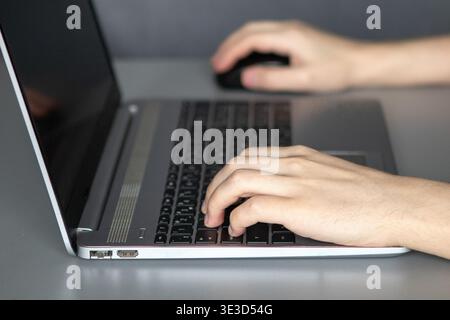 Hands typing on a laptop keyboard with a mouse depicting remote work and digital productivity Stock Photo