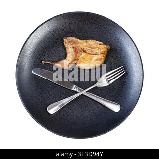 Top view of half of roast quail with crossed fork and knife on black plate, against white background Stock Photo