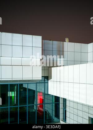 An abstract view of a geometric modern building structure featuring white square panels with green and red lights glowing from below at night. The sce Stock Photo