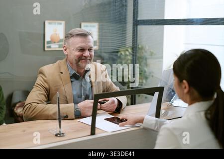 Middle Aged Caucasian Man Smiling While Speaking with Bank Employee at Branch Stock Photo