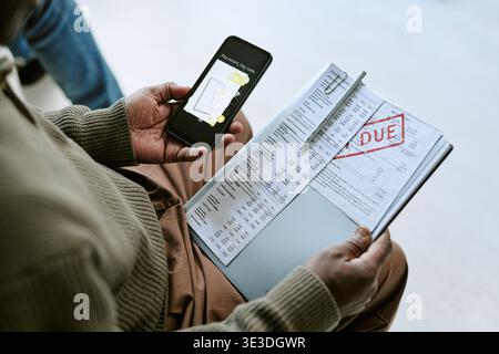 Black Man Using Smartphone While Reviewing Overdue Bank Statement Stock Photo