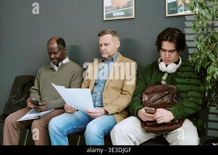 Middle Aged Caucasian Man and Senior Black Man Waiting in Bank Branch Lobby Stock Photo