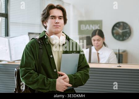 Portrait of Young Caucasian Man Standing in Bank Branch Holding Clipboard Stock Photo
