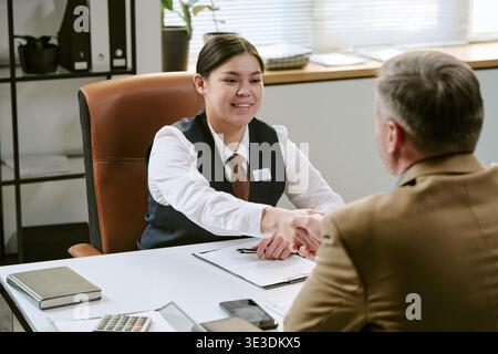 Young Adult Asian Woman Greeting Middle Aged Caucasian Man in Bank Branch Office Stock Photo