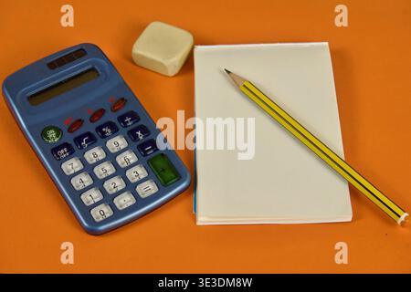 Vintage blue calculator with notepad, pencil, and eraser on an orange background Stock Photo