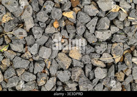 Close-up of gray gravel stones with small pebbles and dried twigs. Surface texture shows rough, uneven, natural material. Ideal for construction, land Stock Photo