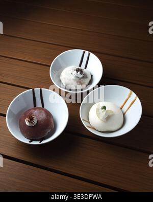 Three delicate desserts sit in white bowls on a wooden table. Each dessert has a unique texture and topping. Simple lines on the bowls add minimalist Stock Photo