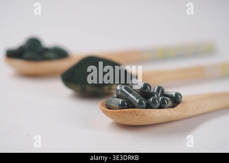 Spoon with green powder and capsules on a white background Stock Photo