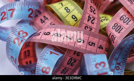 A tangled pile of colorful flexible measuring tapes in pink, blue, and yellow, showing various numerical scales. Close up. Stock Photo