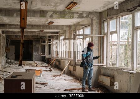 Man standing inside an abandoned building in Chernobyl, looking through broken windows. Black and white style enhances the atmosphere of decay, silenc Stock Photo