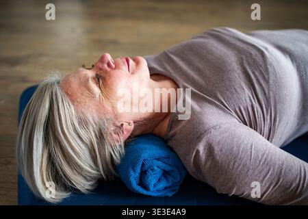 Senior woman relaxing during physiotherapy exercise lying on yoga mat. Stock Photo
