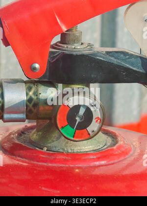 A detailed macro photograph of the pressure gauge and operating handle of a red fire extinguisher. The gauge indicates the device is pressurized and r Stock Photo