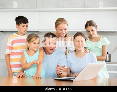Large family is sitting in kitchen next to laptop and making video call to grandparents Stock Photo