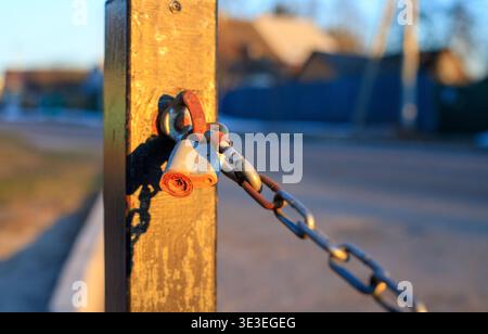 Rusty padlock on a metal chain secured to a post at sunset. Close-up view showcasing security measures, outdoor protection, and the weathered texture Stock Photo