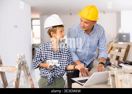 Man architect and boy using laptop while discussing working process in house being renovated Stock Photo