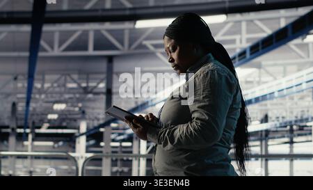 Data center software developers deploy machine learning software on infrastructure racks. Server room IT specialists train AI systems with datasets using tablet to support applications, camera B Stock Photo