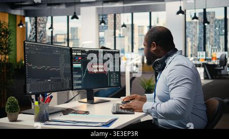 Forex investment consultant investigating suspicious access on trading account. African american man in office worried about security popup on PC about attempted breach of client account Stock Photo