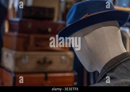 Mannequin head wearing hat in boutique interior with vintage suitcases in background. Fashion retail display and visual merchandising concept with cla Stock Photo