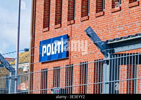 Exterior view of a red brick police station with a blue Danish Politi police sign and a metal security fence topped with barbed wire under a clear sky Stock Photo