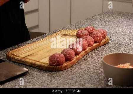 Raw meatballs on wooden cutting board in kitchen preparation scene Stock Photo