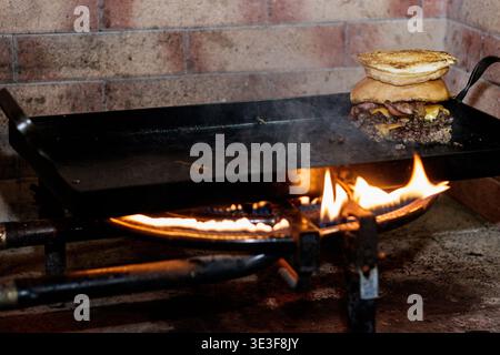A cheeseburger with bacon cooking on a griddle over an open flame Stock Photo