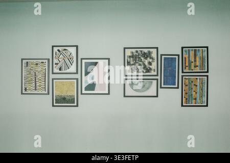 Modern art prints arranged on a light-colored wall. Geometric and abstract patterns fill each framed piece. Varied textures and colors create a balanc Stock Photo