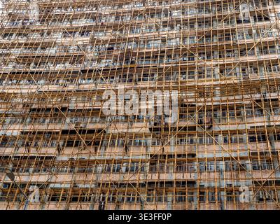 Bamboo scaffolding covering high rise residential building in Hong Kong during renovation. Traditional construction technique used for facade maintena Stock Photo