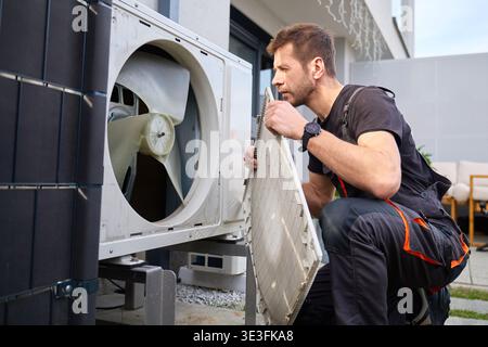 Technician removing front cover and inspecting fan inside outdoor heat pump unit. Concept of HVAC maintenance, repair service and energy efficient hom Stock Photo