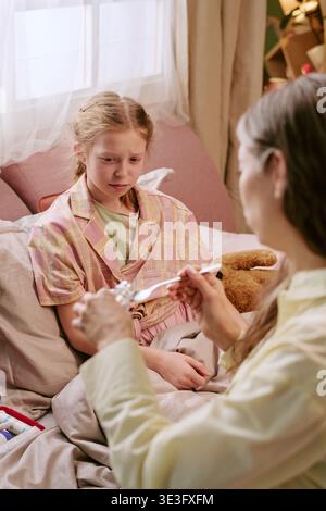 Girl Sitting in Bed Watching Middle Aged Woman Preparing Medicine Stock Photo
