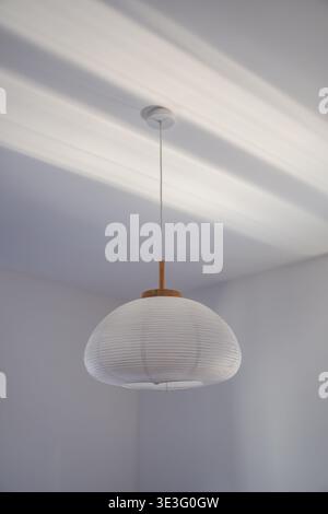 Minimalist hanging ceiling lamp with paper shade casting soft light and shadows on white ceiling, modern home interior detail, selective focus Stock Photo