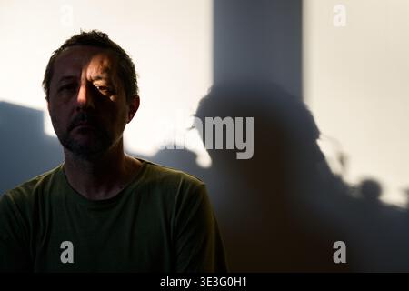 Portrait of a middle-aged man with short dark hair and beard, face half in deep shadow, for human emotion, resilience, urban solitude. Selective focus Stock Photo